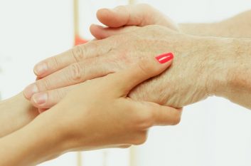The visiting nurse or health visitor taking care of senior man. Lifestyle portrait at home. Medicine, healthcare and prevention. Girl holding patient's hands during the visit. Close up photo.